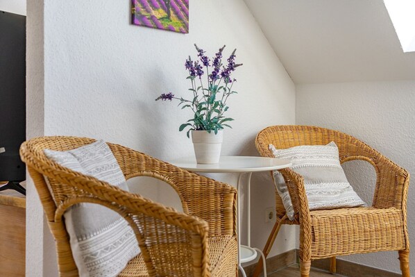 A corner of a room with two wicker chairs, a small table, and a potted plant with purple flowers.