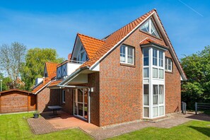 A two-story brick house with a sloped roof, a covered patio, and a visible garage.
