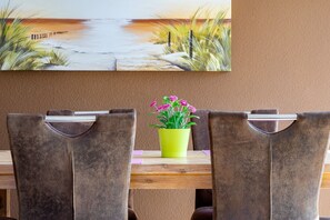 A dining area with two chairs, a wooden table, and a painting of a beach scene above.