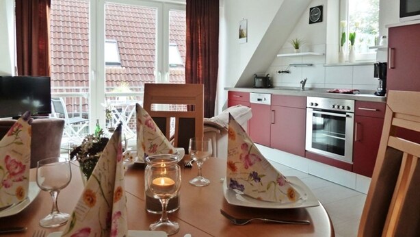 Comedor con una mesa lista para cuatro, un televisor y una cocina al fondo.