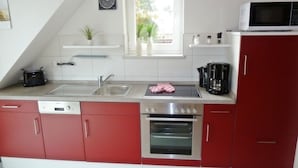 Una cocina con armarios rojos, un lavamanos de acero inoxidable, un microondas y un horno.