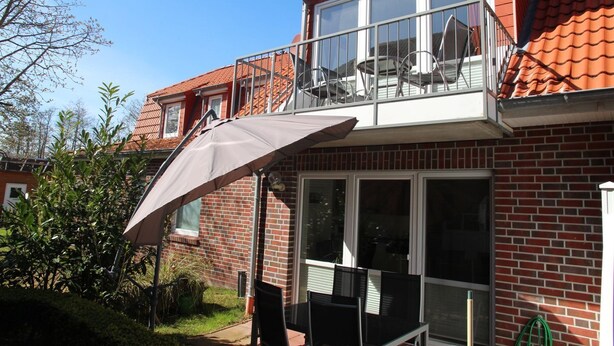 Ein zweigeschossiges Haus mit Balkon, großem Fenster und einer Terrasse mit Tisch und Stühlen.