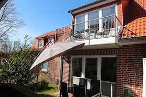 Ein zweigeschossiges Haus mit Balkon, großem Fenster und einer Terrasse mit Tisch und Stühlen.