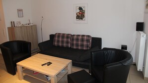 Ein Wohnzimmer mit einer schwarzen Couch, zwei schwarzen Sesseln, einem Holztisch und einem kleinen Beistelltisch.