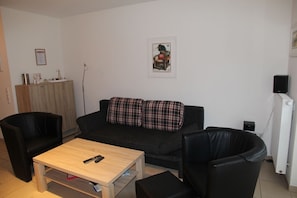 Una sala de estar con un sofá negro, dos sillones negros, una mesa de centro de madera y una mesita auxiliar.