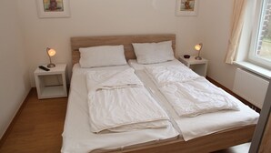 Ein ordentlich bezogenes Doppelbett mit weißen Leinen, zwei Nachttische mit Lampen und zwei gerahmte Bilder an der Wand.