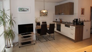 Eine moderne Küche mit weißen Schränken, ein Essbereich mit Fernseher und Stühlen sowie ein Blumentopf.