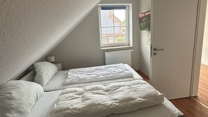 Et soveværelse med skråvæg, et vindue med rullegardiner, en radiator og en dør.