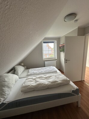 A bedroom with a sloped ceiling, a window with blinds, a radiator, and a door. - Sieloase - End terraced house in a quiet location with water access (Krummhörn)