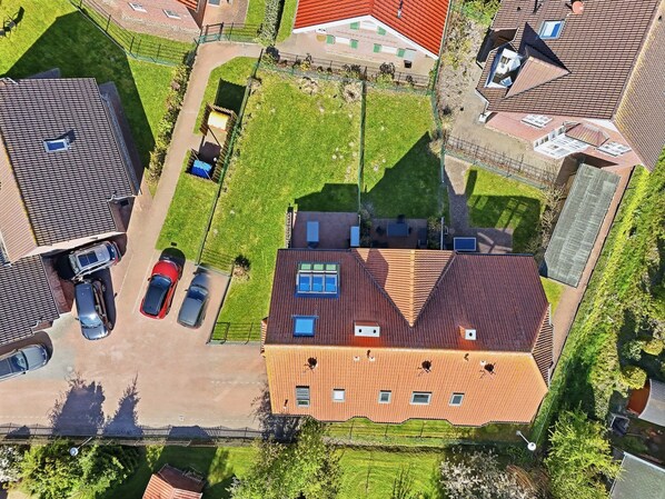 An aerial view of a residential area with a house featuring a sloped roof, multiple windows, and a fenced yard.