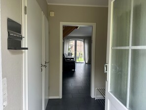 A hallway with a door on the left, a window on the right, and a view of a living area with a sofa and a table.
