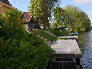 A riverside property with a wooden dock, steps leading to a house, and lush greenery.