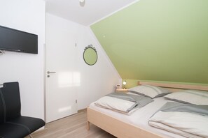 A bedroom with a bed, a chair, a desk, a wall-mounted TV, and a door. - Ferijentied - Kinderfreundliches Ferienhaus in Zentraler Lage (Krummhörn)