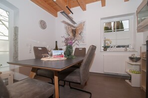 A dining area with a table set for two, a clock on the wall, and a window with blinds. - Ferijentied - Kinderfreundliches Ferienhaus in Zentraler Lage (Krummhörn)