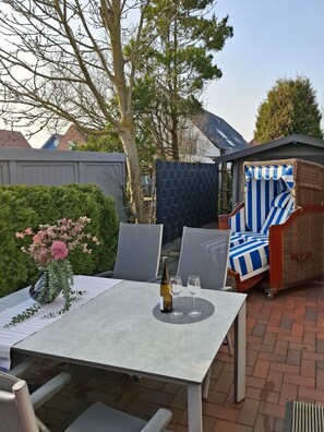 A patio with a table, chairs, a bottle of wine, and a striped chair. - Ferijentied - Kinderfreundliches Ferienhaus in Zentraler Lage (Krummhörn)