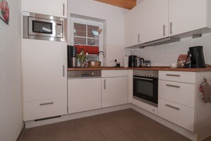 Una cocina moderna con armarios blancos, horno integrado, microondas y cafetera.