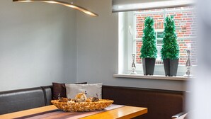 A modern room with a wooden table, a cushioned bench, and a window with two potted plants. - Haus Otter - Beautiful vacation home (100sqm) for 6 persons and dog with fireplace, sauna (Norden)