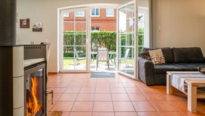 A living room with a fireplace, a sofa, and a glass door leading to a patio with a table and chairs. - Haus Otter - Beautiful vacation home (100sqm) for 6 persons and dog with fireplace, sauna (Norden)