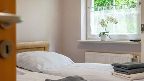 A bedroom with a bed, a window with a view of greenery, a radiator, and a small shelf with a plant. - Haus Otter - Beautiful vacation home (100sqm) for 6 persons and dog with fireplace, sauna (Norden)