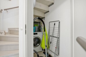 A laundry room with a washing machine, a drying rack, and a step with a handrail.