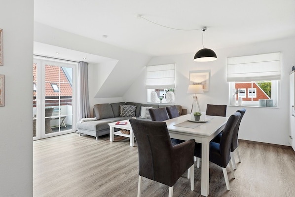 A modern living room with a sofa, dining table, chairs, and a ceiling light.