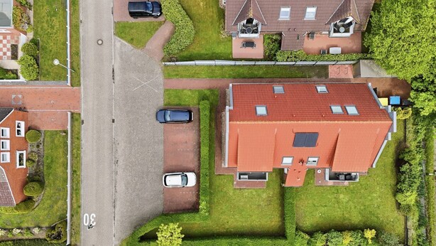 An aerial view of a residential area with houses, a street, and parked cars.