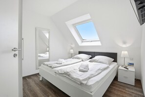 Ein Schlafzimmer mit Dachfenster, einem Bett mit weißer Bettwäsche, einem Nachttisch mit Lampe und einem Spiegel.