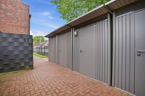 A pathway leading to a building with grey metal doors and a brick wall. - Deichbude - Deichbude Greetsiel: 75 m² vacation apartment with balcony, WLAN & (Krummhörn)