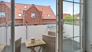 A balcony with wicker furniture, a small table, and a view of a red-roofed building.