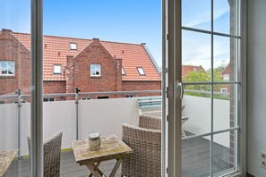 Ein Balkon mit Korbmöbeln, einem kleinen Tisch und Blick auf ein Gebäude mit rotem Dach.