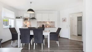 A modern kitchen with white cabinets, a dining table with chairs, and a hanging light fixture.