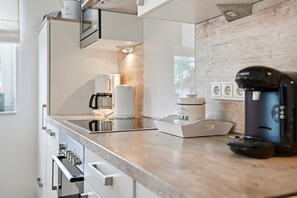 A modern kitchen with a built-in oven, a coffee maker, and a sugar container on the counter. - Deichbude - Deichbude Greetsiel: 75 m² vacation apartment with balcony, WLAN & (Krummhörn)