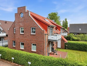 Une maison en briques rouges, avec un toit en pente, un balcon et un petit jardin.
