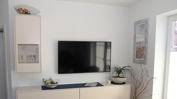 Een woonkamer met een flatscreen televisie aan de muur, een witte console tafel met decoratieve objecten en een potplant.
