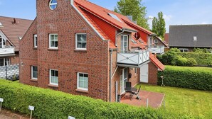 Een huis met rode bakstenen, een schuin dak, een balkon en een kleine tuin.