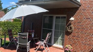 Een terras met twee stoelen, een tafel en een witte parasol.