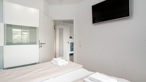 Ein Schlafzimmer mit Bett, einem an der Wand montierten Fernseher und einem durchgehenden Türrahmen einsehbarer Badezimmer.