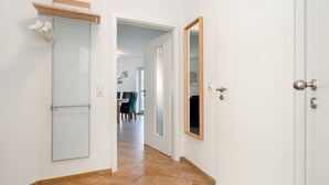 Ein Flur mit Holzboden, einer weißen Tür, einem Spiegel und einem Kleiderhaken mit Kleidung.