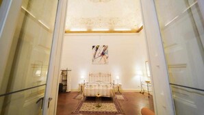 A bedroom with a bed, two bedside tables, a nightstand, a rug, and a ceiling with a decorative pattern. - Neapolitan House - Culture Apartament (Napoli)
