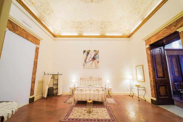A spacious bedroom with a large bed, a ceiling with intricate designs, and a painting on the wall.