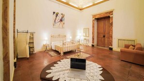 A spacious room with a bed, bedside tables, a laptop on a decorative doily, a sofa, and a large wooden door. - Neapolitan House - Culture Apartament (Napoli)