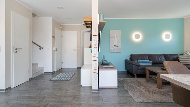 A modern living room with a sofa, coffee table, and a dining area. There is a staircase leading to another room.