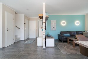 Uma sala de estar moderna com sofá, mesa de centro e área de jantar. Existe uma escada que leva a outro cômodo.