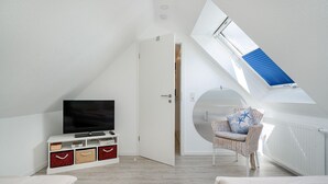A modern room with a TV on a white cabinet, a wicker chair, and a skylight.