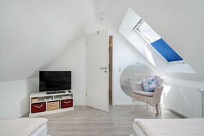 Una habitación moderna con televisión sobre un mueble blanco, una silla de mimbre y un tragaluz.
