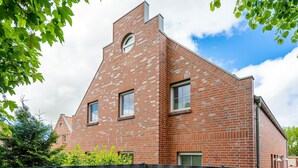 A modern brick building with a triangular roof, two windows, and a black metal fence in front.