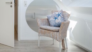 A wicker chair with a cushion and a star-patterned pillow, a white door, and a white wall with a circular window.