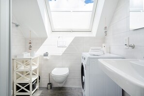 A compact, modern bathroom with a skylight, a washing machine, a toilet, and a sink.