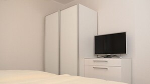 A bedroom with a bed, a TV on a stand, and a wardrobe. - Fiete - Beautiful vacation home directly in the village center! (Krummhörn)