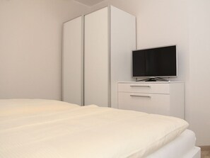A bedroom with a bed, a TV on a stand, and a wardrobe. - Fiete - Beautiful vacation home directly in the village center! (Krummhörn)
